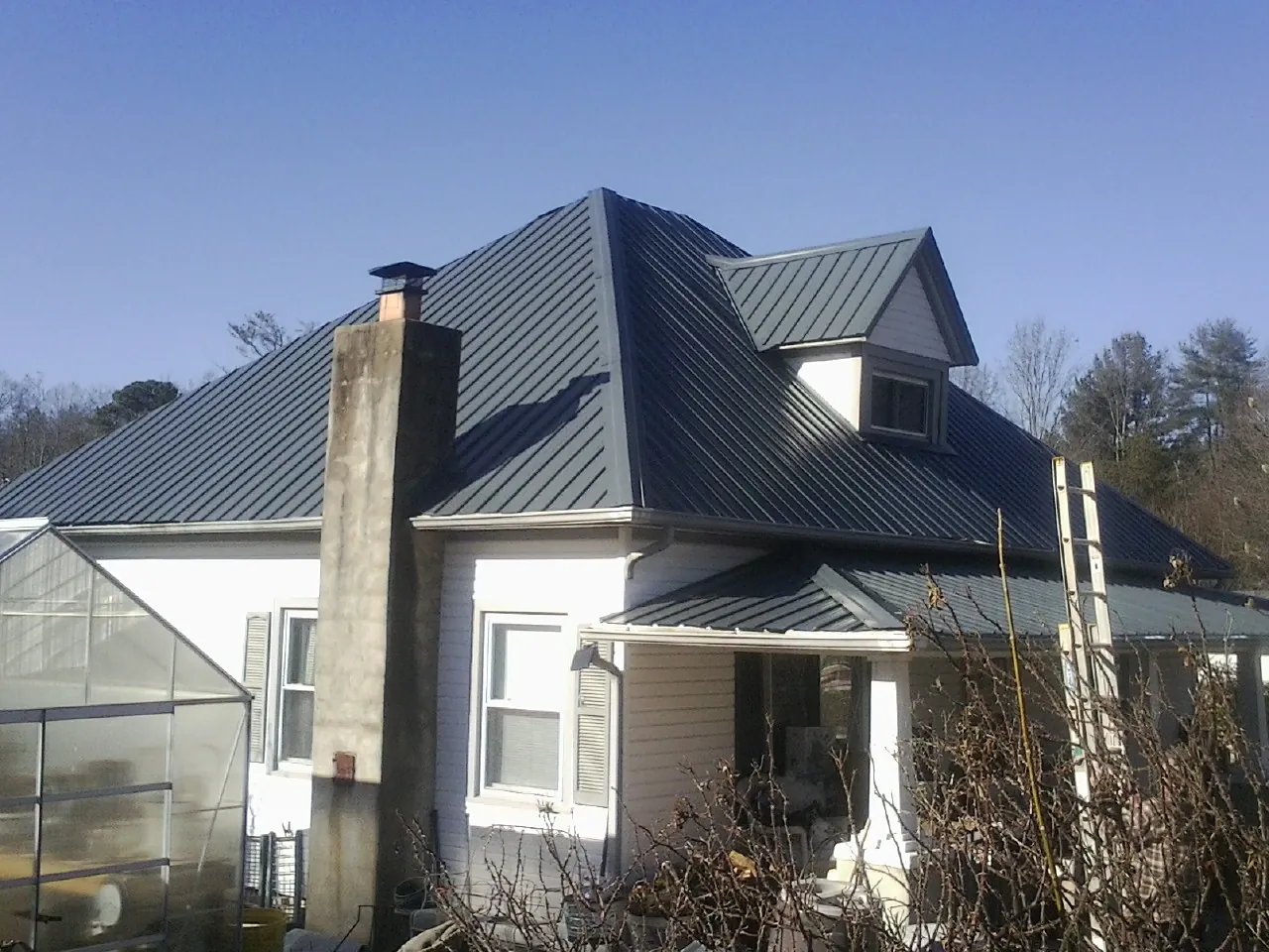 Dark blue standing seam metal roof on a white farmhouse with dormer — Slate & Tile Roof Repair by Roofing Brothers in Glen Ridge