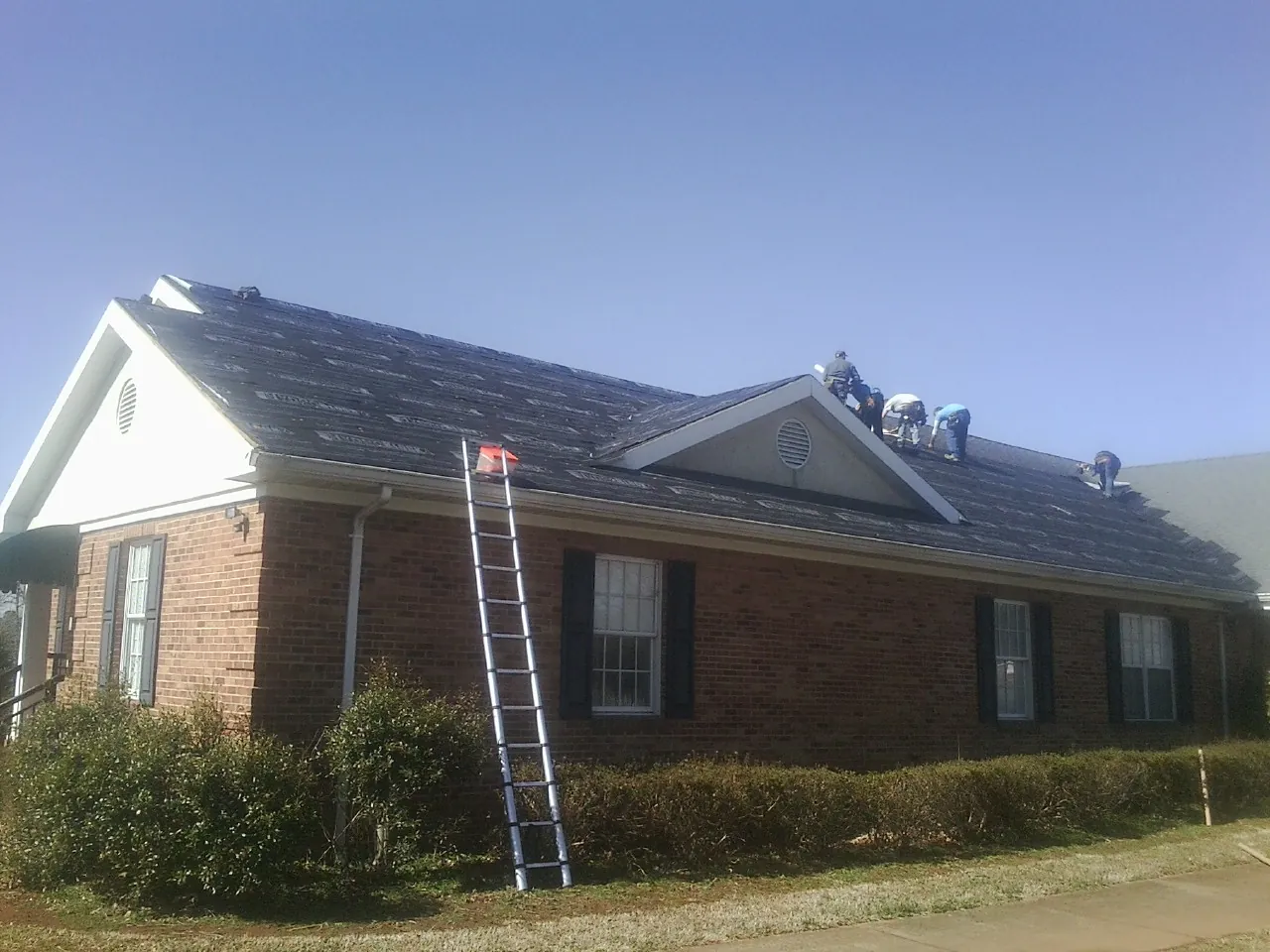 Crew tearing shingles off a brick ranch roof with a ladder set — Emergency Roof Repair work by our crew in Glen Ridge