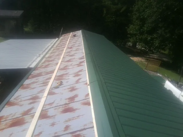 Old rusted panels beside newly installed green metal roofing — Wind Damage Roof Repair by Roofing Brothers in Glen Ridge