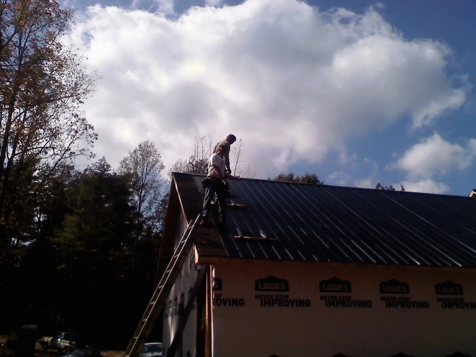 Roofer fastening dark metal panels high against a cloudy sky, from a Roof Inspection job in Glen Ridge