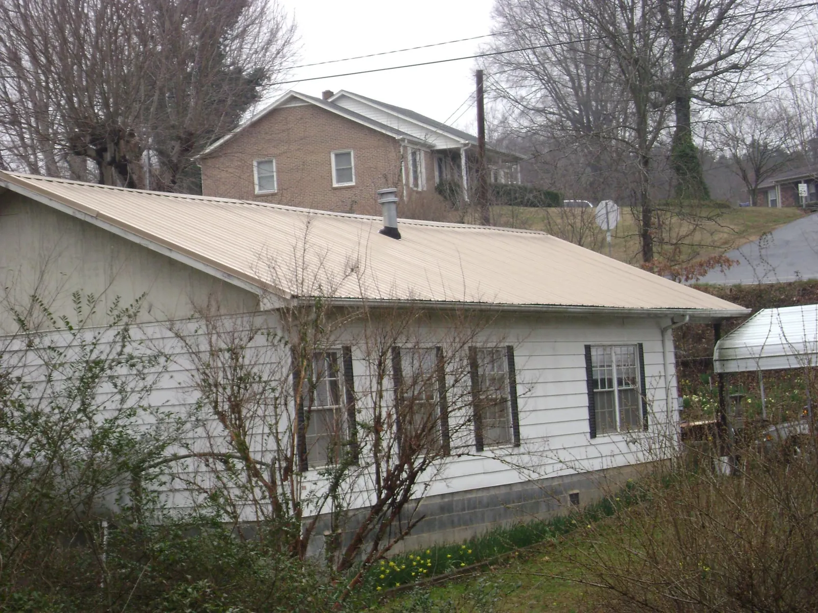 Tan metal roof on a white sided house set into a hillside — Commercial Roofing by Roofing Brothers in Glen Ridge